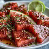 Bright red watermelon wedges sprinkled with Tajin and lime create a vibrant, tangy treat bursting with Mexican-inspired flavor.  