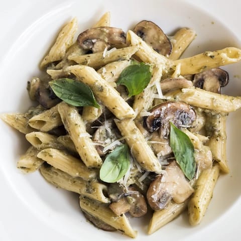 A close-up of Mushroom Pesto Pasta, featuring al dente penne coated in rich, emerald-green pesto and tender, caramelized mushroom slices.
