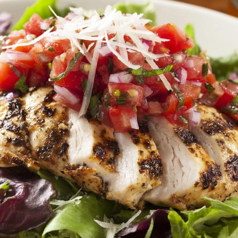 Sliced grilled chicken rests on mixed greens, topped with a vibrant bruschetta chicken salad of tomatoes, basil, and balsamic.