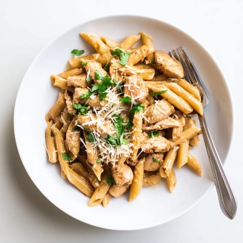 A close-up of creamy Honey Chipotle Chicken Pasta reveals smoky chipotle flecks in the velvety sauce clinging to each penne noodle.