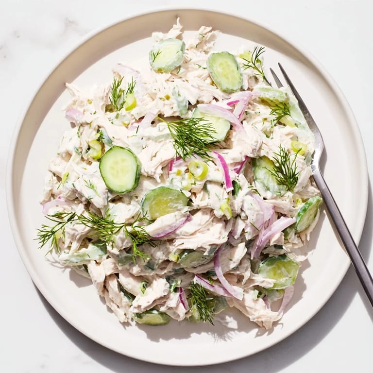 Close-up view of creamy cucumber chicken salad ingredients: diced chicken breast, thinly sliced cucumbers, and red onion mixed in a creamy Greek yogurt dill dressing, ready to serve as a protein-packed lunch.