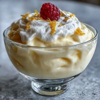 Freshly made Lemon Fool in a glass with lemon zest and raspberries, offering a cool, creamy, and zesty bite.